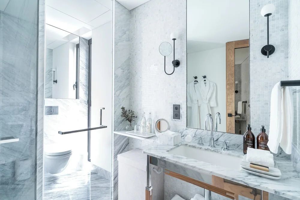 Helles Badezimmer mit Marmorwaschtisch, großem Spiegel, Wandleuchte und Toilette.