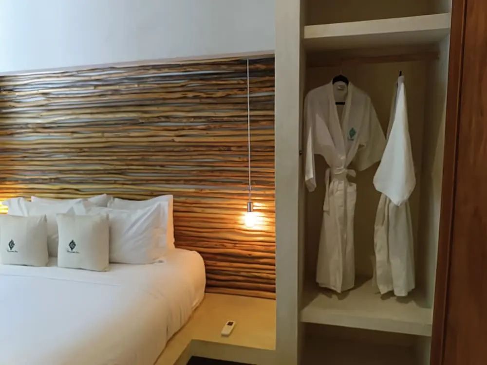 Doppelbett mit Holzkopfteil und offenem Kleiderschrank mit zwei weißen Bademänteln.