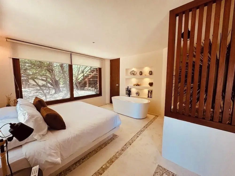 Modernes Schlafzimmer mit weißem Doppelbett, großer Badewanne und beleuchteter Wanddekoration.