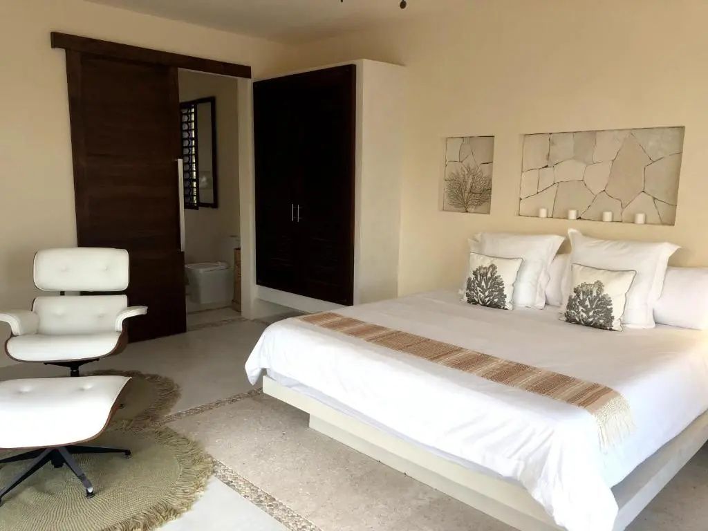 Helles Hotelzimmer mit großem Doppelbett, weißer Bettwäsche, Holzschrank und Blick zum Bad.