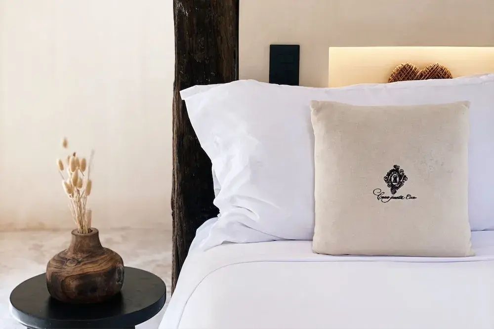 Nahaufnahme eines weiß bezogenen Bettkissens mit gesticktem Logo auf einem hellen Bett.