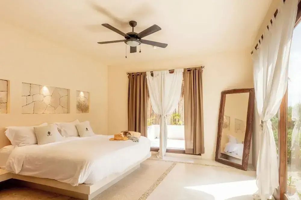 Helles Hotelzimmer mit großem Doppelbett, Deckenventilator, großem Standspiegel und Zugang zur Terrasse.