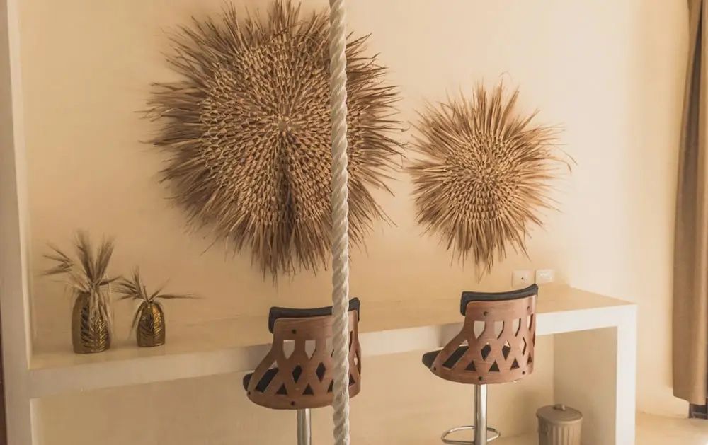 Wanddekoration aus Naturfasern über zwei Holzstühlen an einer hellen Theke.