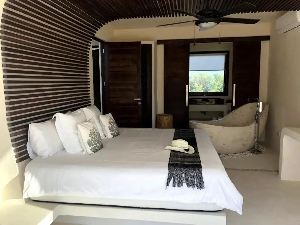 Doppelbett mit Kissen und Hut in einer Suite mit Holzdecke und freistehender Badewanne im Hintergrund.