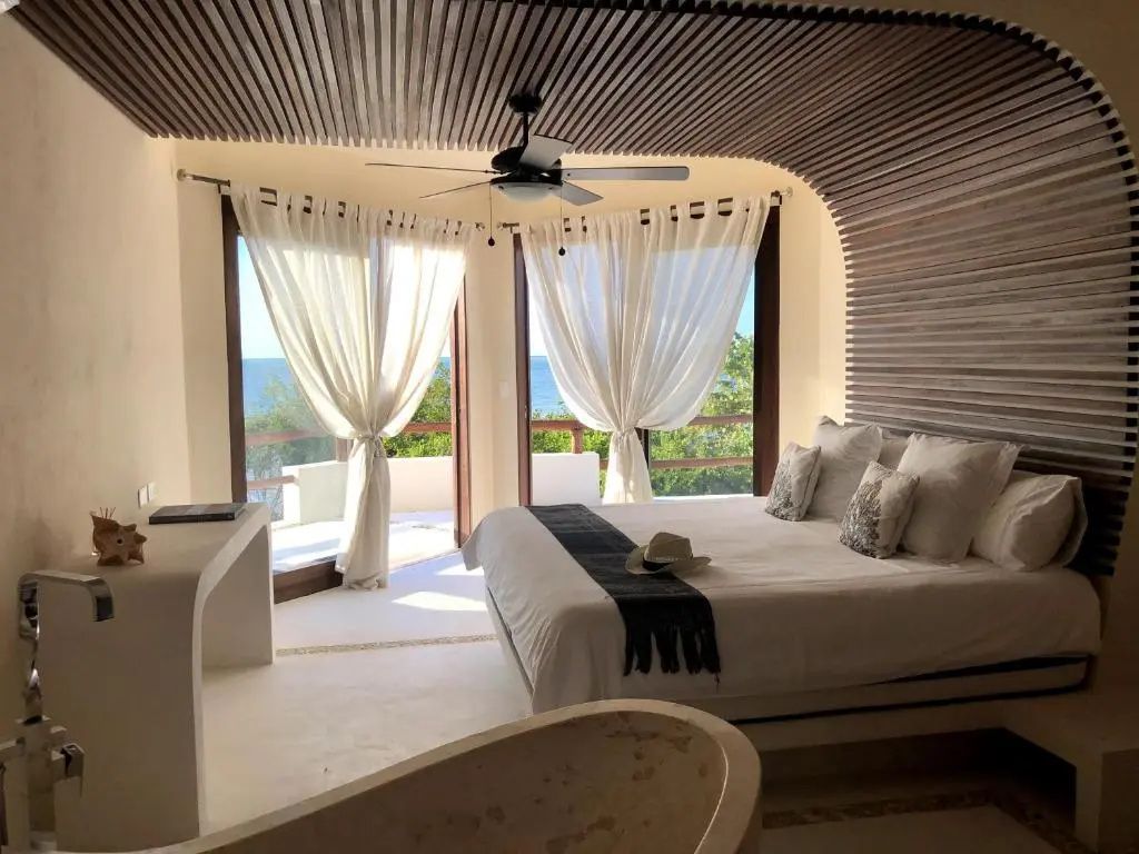 Helles Hotelzimmer mit großem Doppelbett, Holzverkleidung an der Decke und Meerblick.