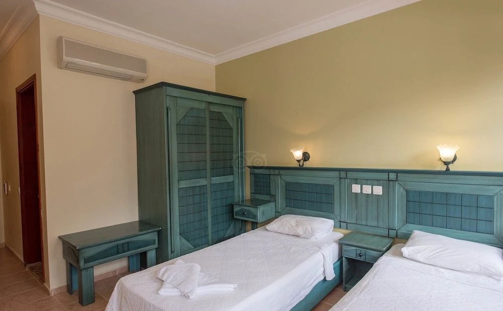 Hotelzimmer mit zwei Einzelbetten, grünen Holzmöbeln und einer Klimaanlage.