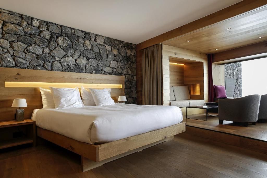 Hotelzimmer mit hölzernem Doppelbett, Natursteinwand und Holzverkleidung sowie Sitzecke.