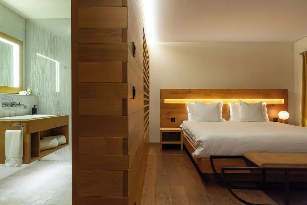 Modernes Hotelzimmer mit Holzverkleidung, Doppelbett, Deckenbeleuchtung und Blick ins Bad.
