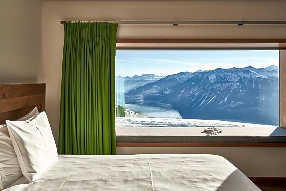Blick durch ein großes Fenster im Hotelzimmer auf verschneite Bergketten.