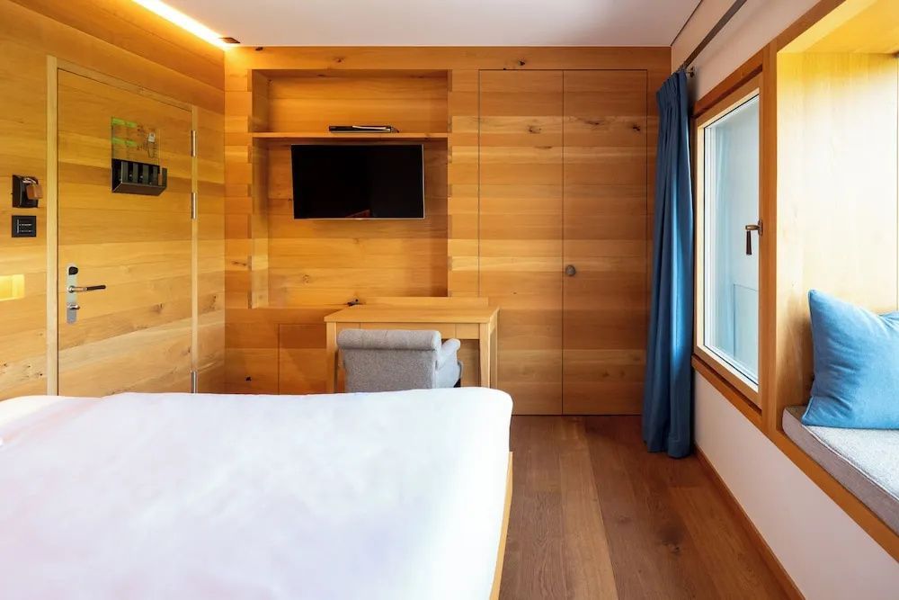 Holzverkleidetes Hotelzimmer mit Flachbildfernseher, Schreibtisch und blauem Vorhang.