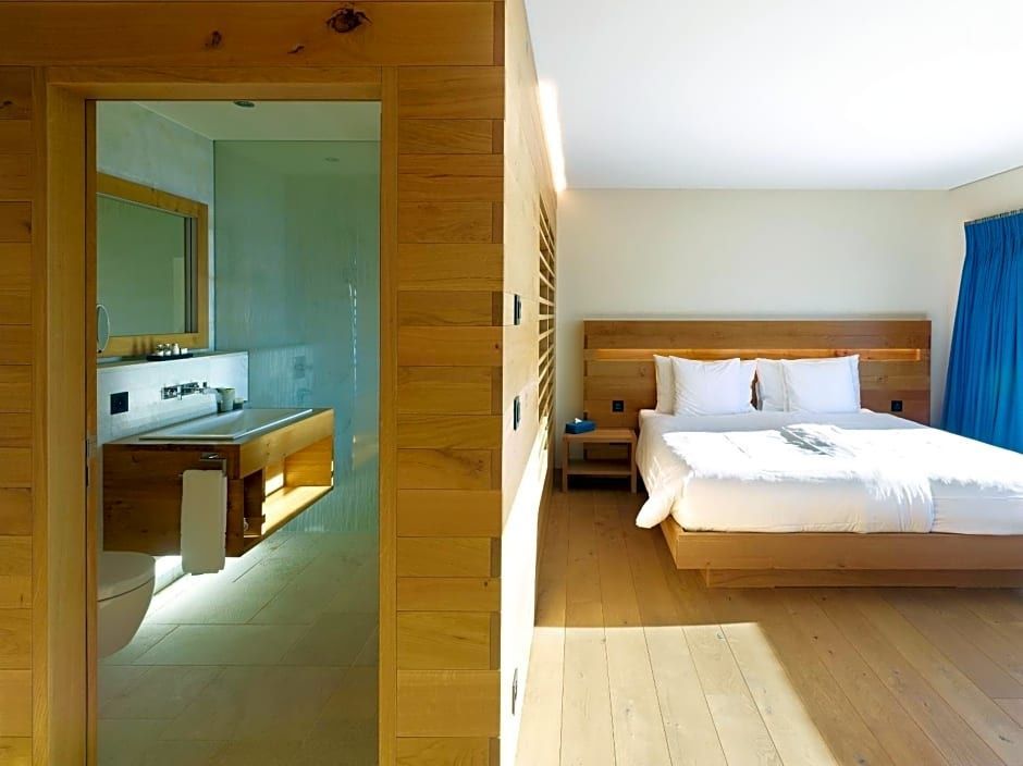 Helles Hotelzimmer mit Holzverkleidung, Doppelbett und angrenzendem Bad.