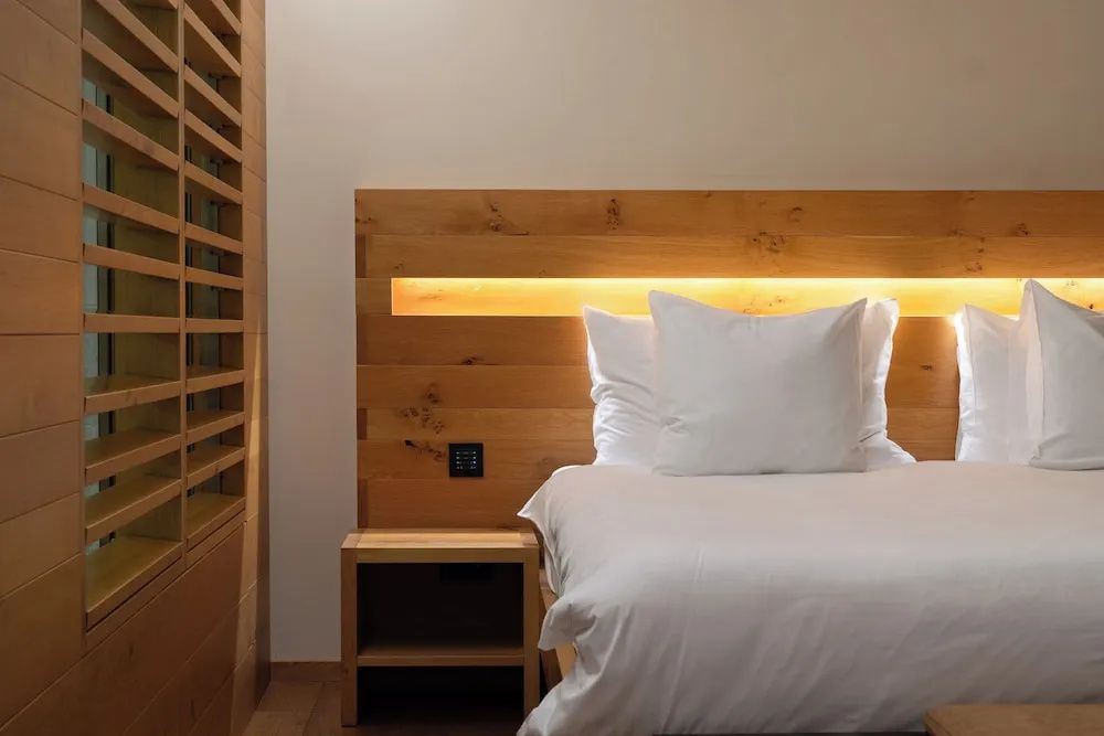 Bett mit Kopfteil aus Holz, integrierter Beleuchtung und einem Nachttisch.