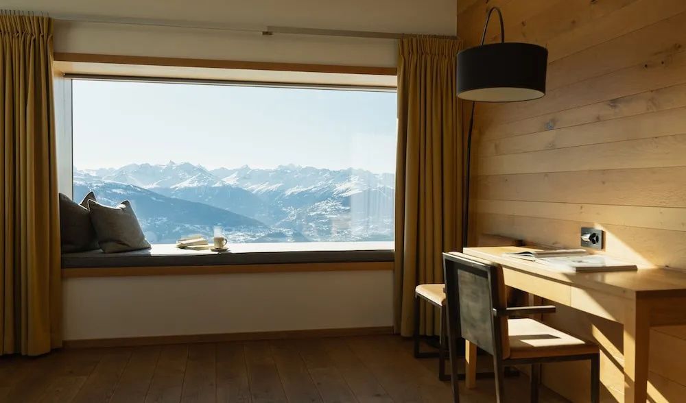 Sitzfenster im holzverkleideten Zimmer mit Blick auf die verschneiten Bergspitzen.