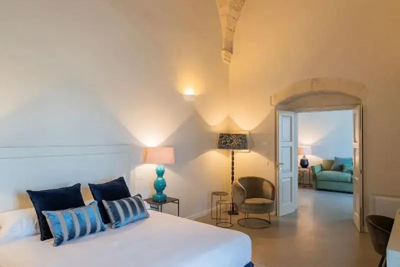 Schlafzimmer mit Doppelbett, blauen Kissen, Sessel und Bogenarchitektur unter Gewölbedecke.