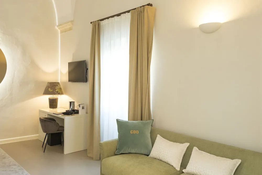 Sitzbereich im Hotelzimmer mit grünem Sofa, Vorhängen und einem Schreibtisch.