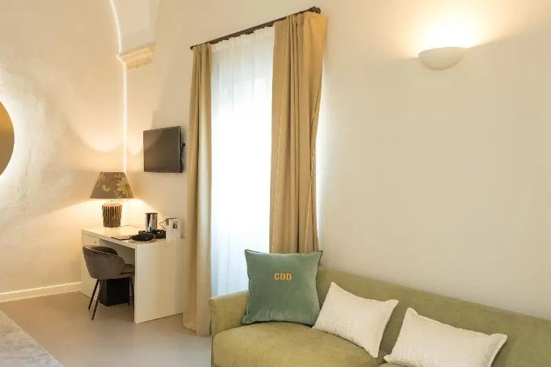 Sitzbereich im Hotelzimmer mit grünem Sofa, Kissen und Schreibtisch am Fenster.
