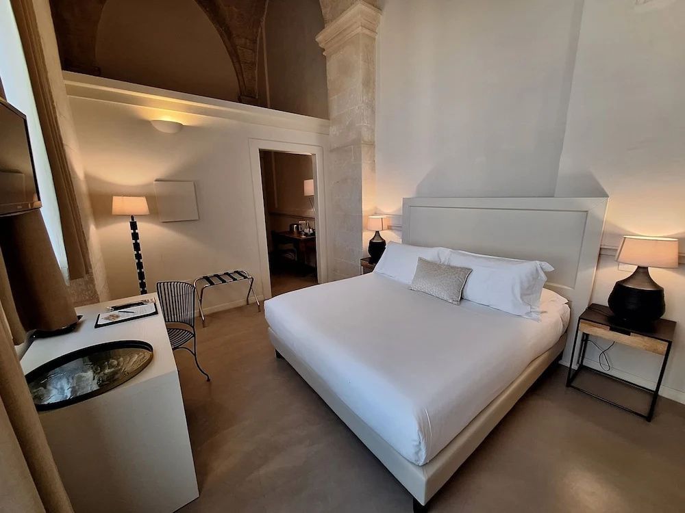 Hell eingerichtetes Zimmer mit Gewölbedecke, großem Doppelbett und Schreibtisch.