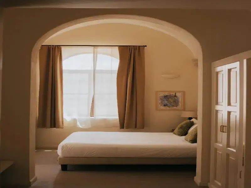Blick durch einen Rundbogen auf ein Hotelzimmer mit Doppelbett und Rundbogenfenster.