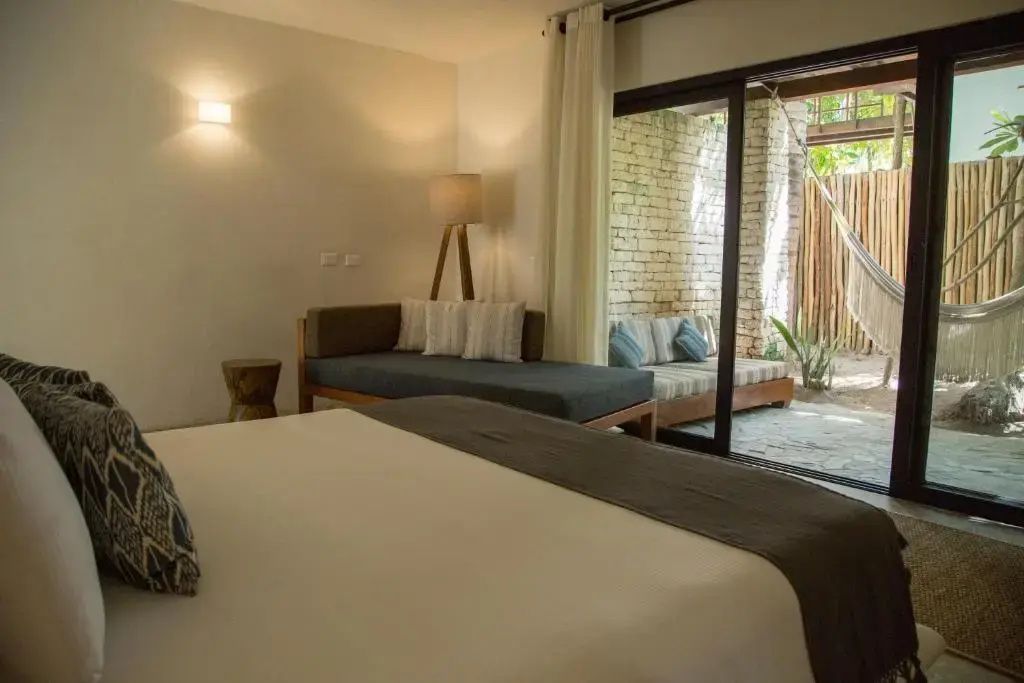 Hell eingerichtetes Hotelzimmer mit Tagesbett und Zugang zur privaten Terrasse mit Hängematte.