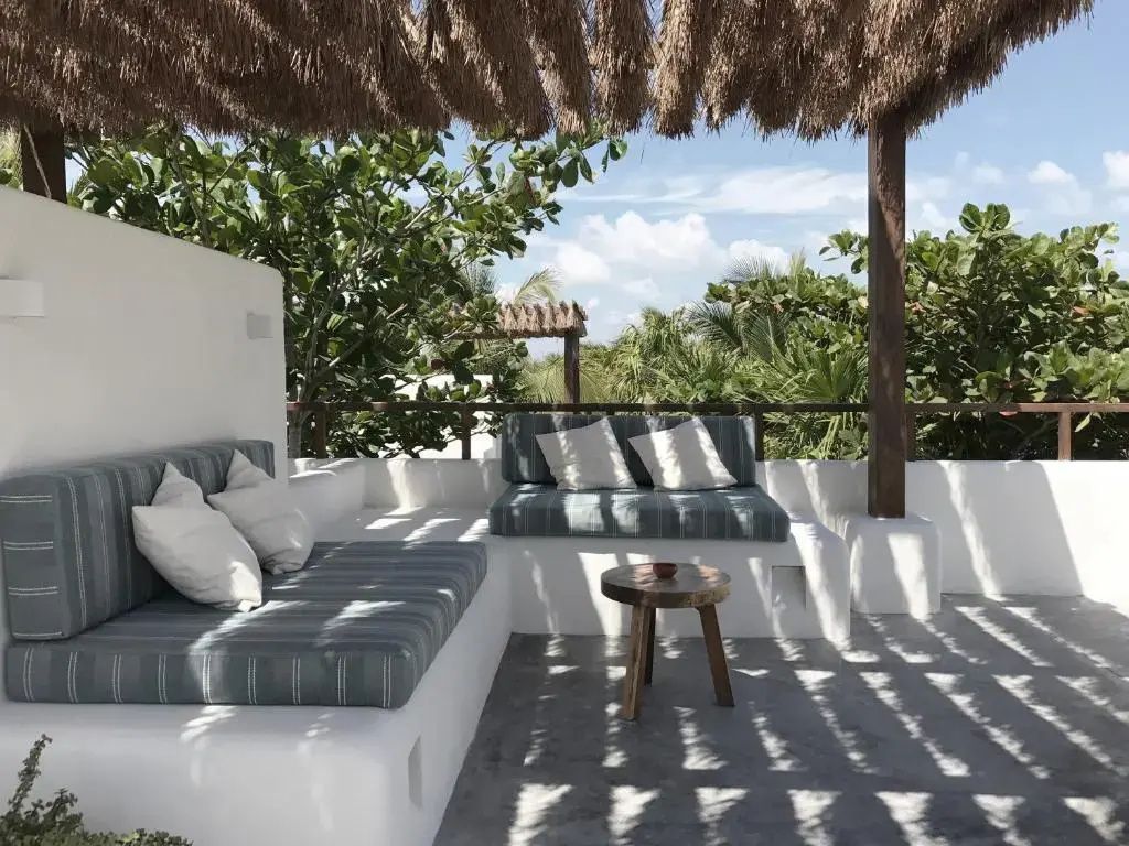 Überdachte Terrasse mit weiß gemauerten Sitzbänken, Polstern und Holzcouchtisch.