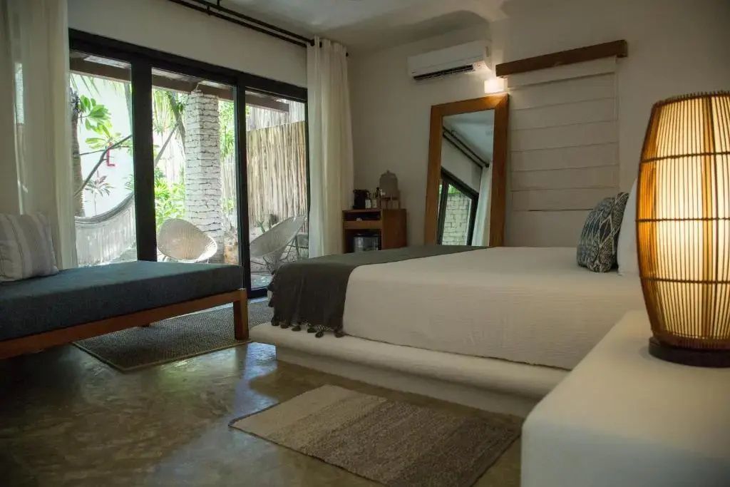 Hotelzimmer mit großem Bett, Standspiegel aus Holz und Schiebetür zum Außenbereich.