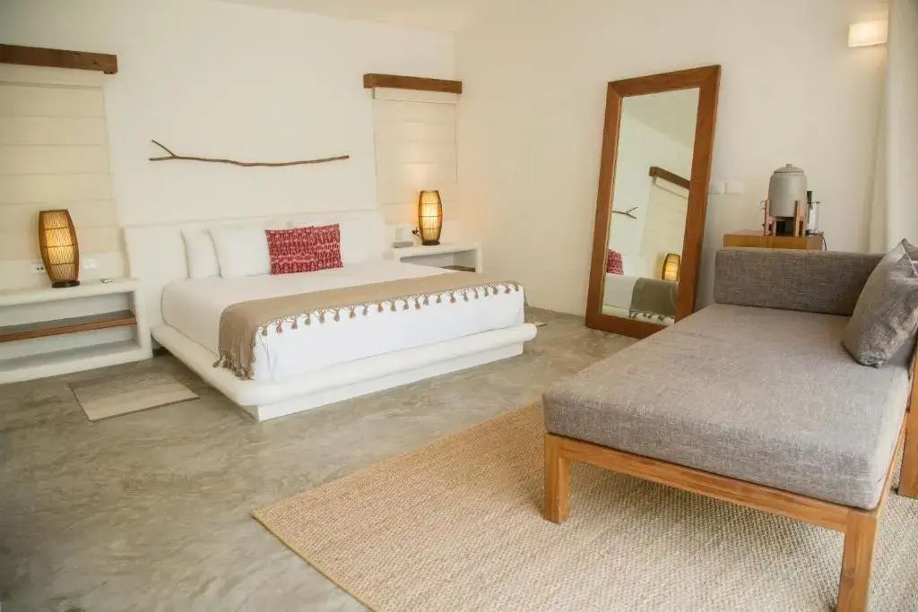 Helles Hotelzimmer mit großem Doppelbett, Ganzkörperspiegel und Holzmöbeln.