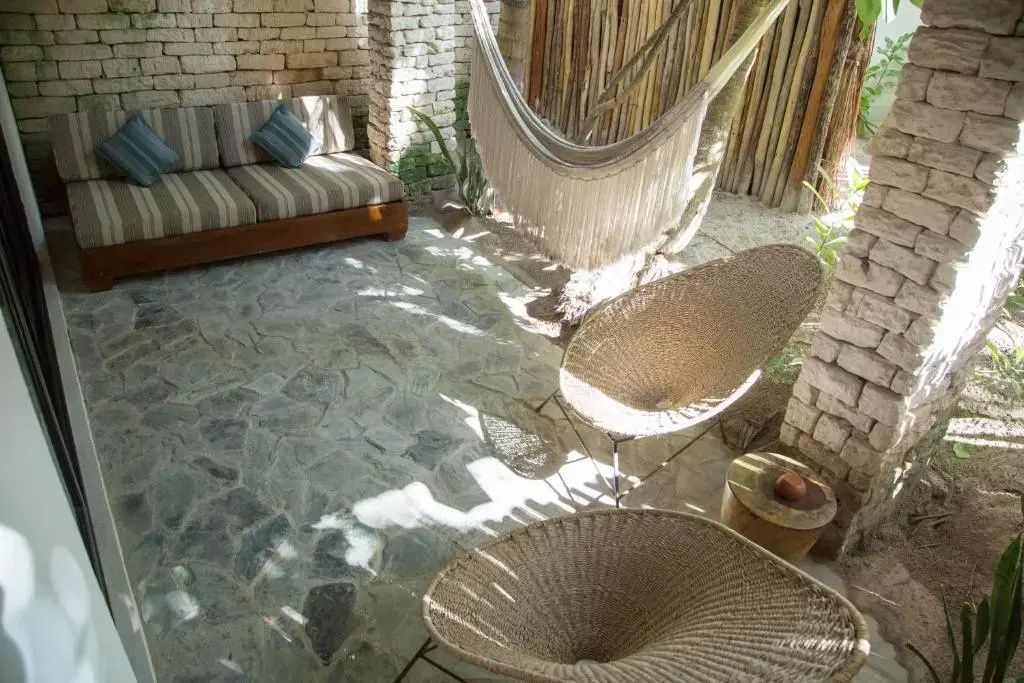 Überdachte Terrasse mit Hängematte, geflochtenen Sesseln und Steinboden im Außenbereich.