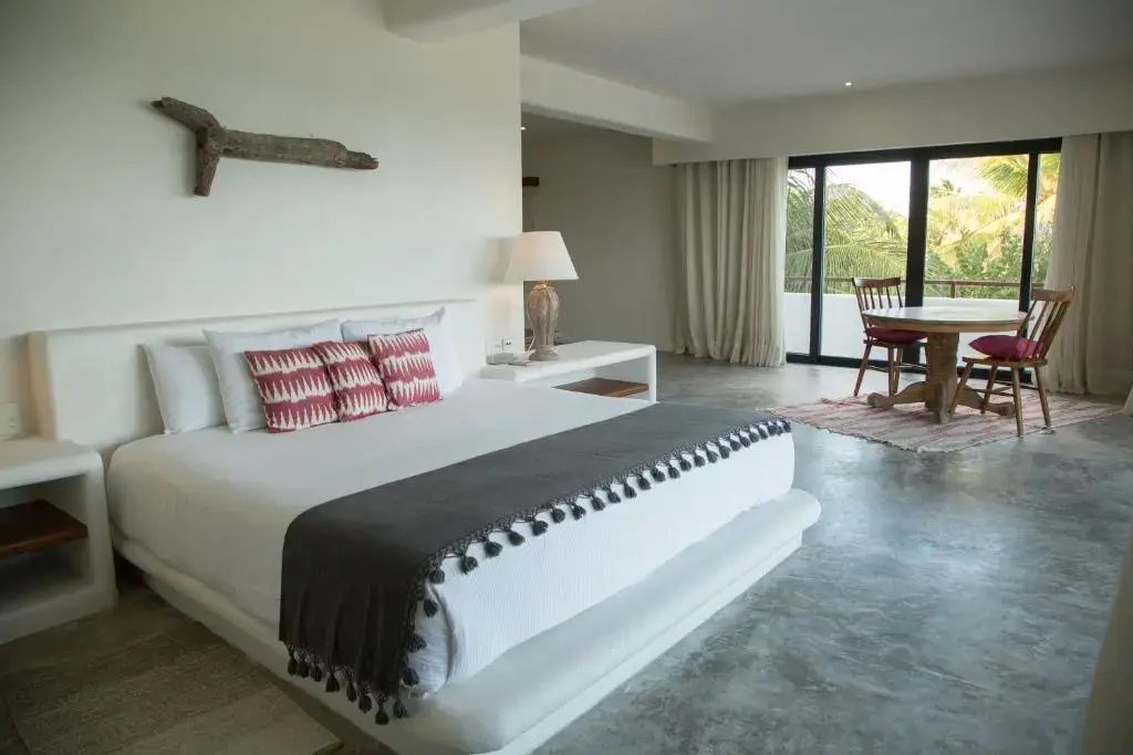 Helles Hotelzimmer mit großem Doppelbett, Holzdekoration an der Wand und Zugang zum Balkon.