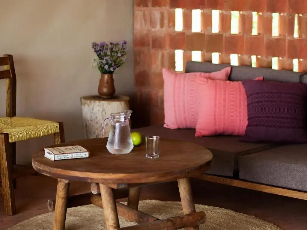 Holztisch mit Glaskaraffe und Buch neben einer Couch mit rosa Kissen