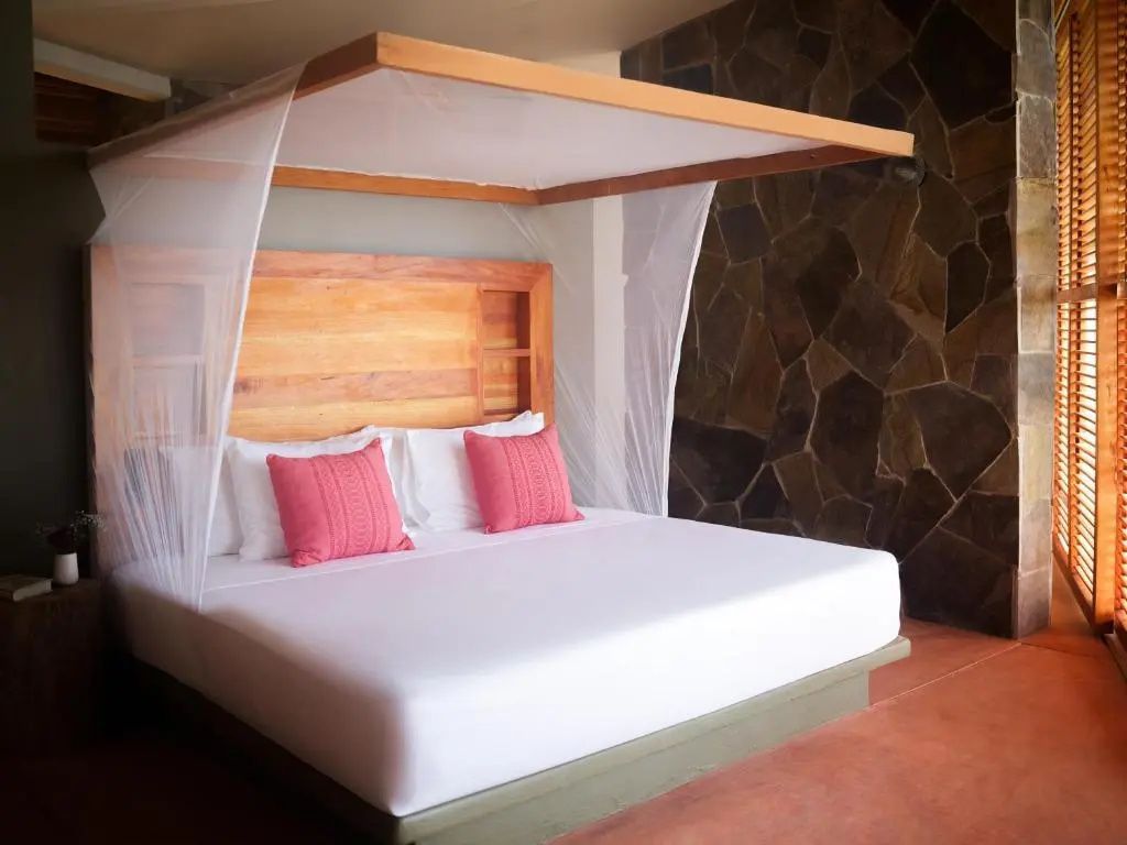 Doppelbett mit Holzrahmen, rosa Kissen und weißem Moskitonetz