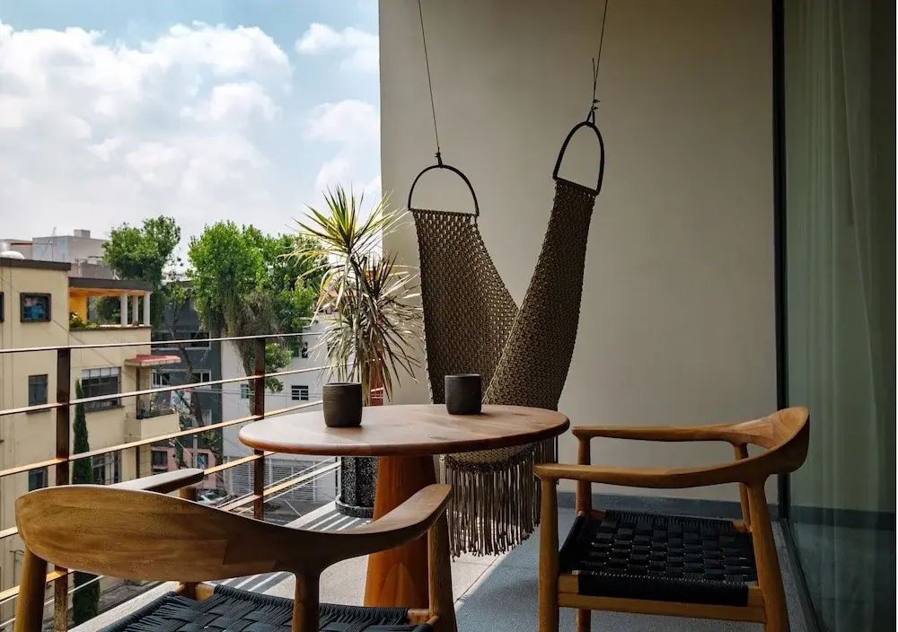 Balkon mit Holzsitzmöbeln, runden Tischen, Hängesessel und Blick auf Stadt und Bäume.