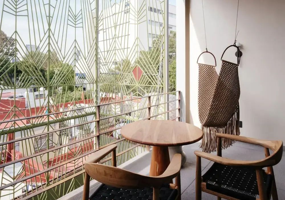 Balkon mit rundem Holztisch, zwei Stühlen und einem kunstvollen grünen Metallgitter.