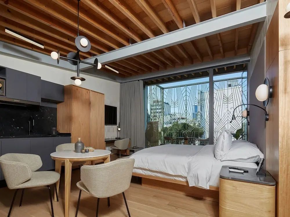 Modern eingerichtetes Zimmer mit Holzdecke, Esstisch, Doppelbett und großem Fenster zum Balkon.