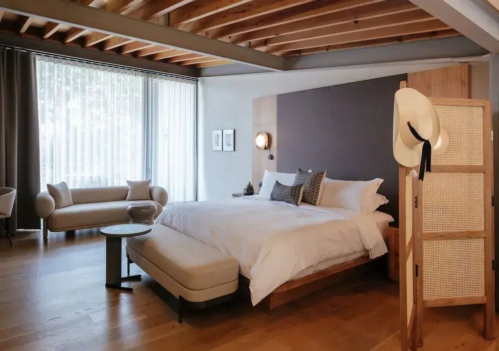 Hotelzimmer mit großem Bett, beigefarbenem Sofa und Holzdecke im modernen Design.