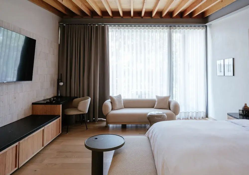 Sitzecke im Hotelzimmer mit hellen Vorhängen, beigem Sofa und Schreibtisch.
