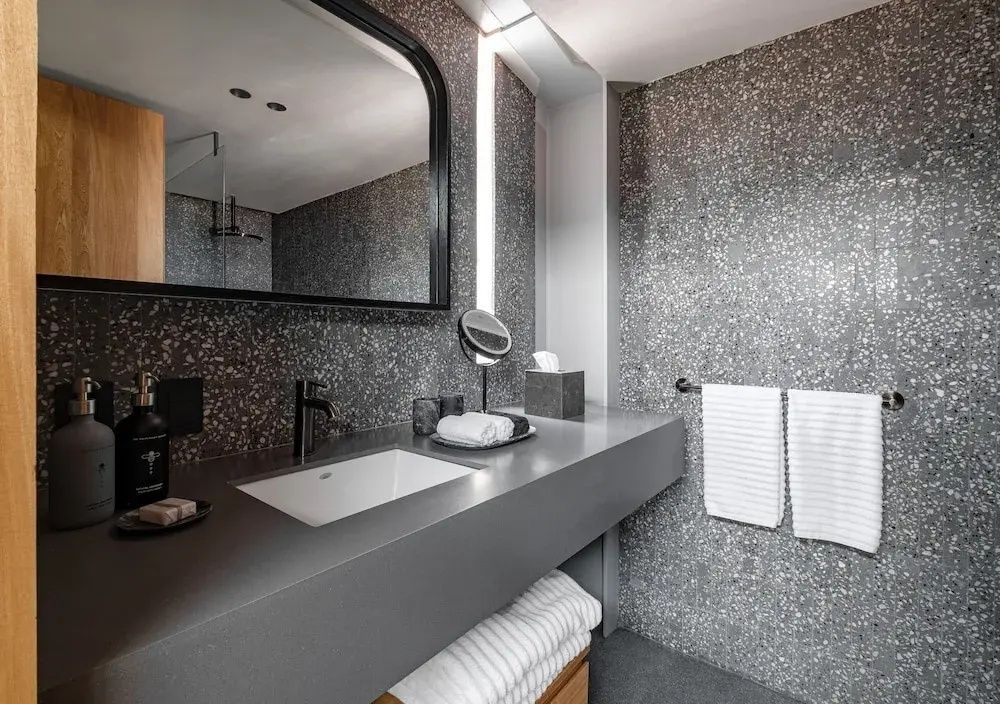 Badezimmer mit grauer Terrazzo-Wand, großem Spiegel, Waschtisch und Handtüchern.