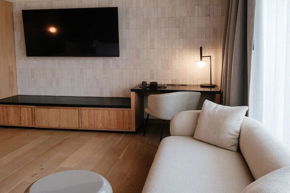 Wohnbereich mit einem Sessel, einem Schreibtisch samt Lampe und einem Fernseher an der Wand.