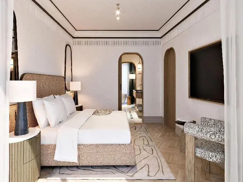 Helles Hotelzimmer mit Doppelbett, Flachbildfernseher und Rundbogendurchgang zum Badezimmer.