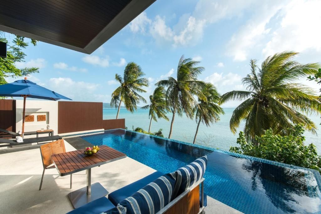 Terrasse einer Villa mit blauem Infinity Pool, Sitzbereich, Palmen und Meerblick.