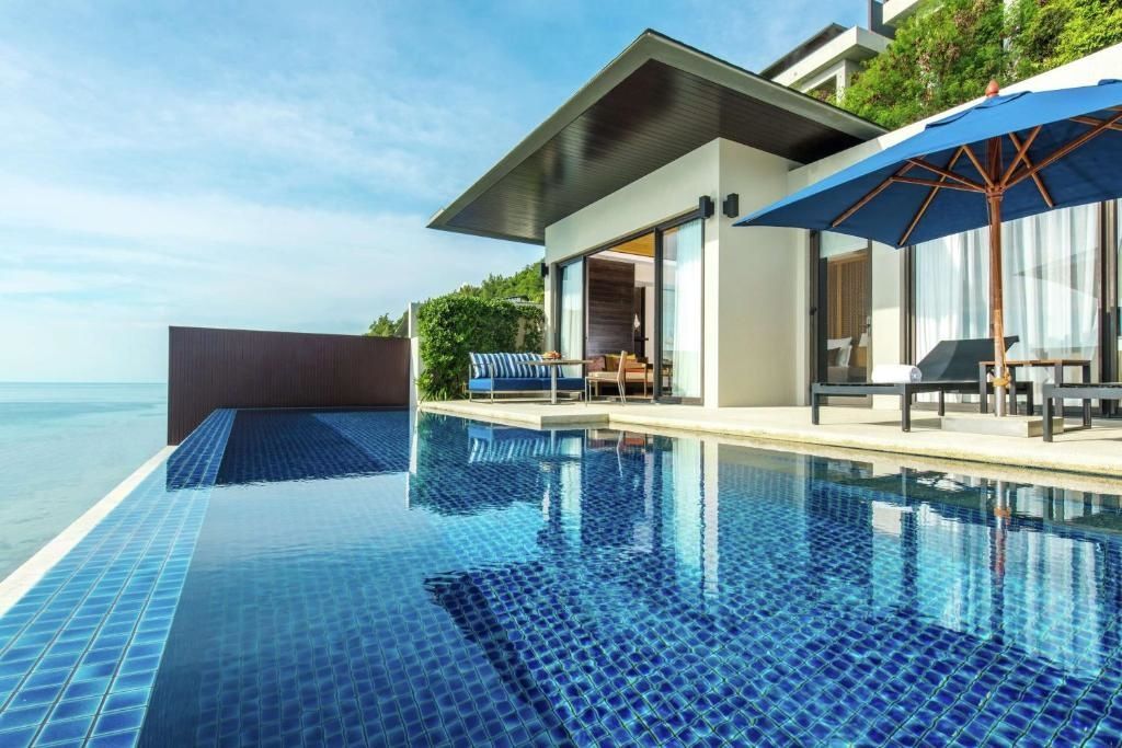 Blau gefliester Pool auf der Terrasse einer Villa mit Liegestühlen und einem Sonnenschirm.