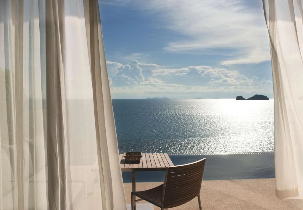 Blick von einer überdachten Terrasse mit Sitzgelegenheit auf das ruhige Meer und den Horizont.
