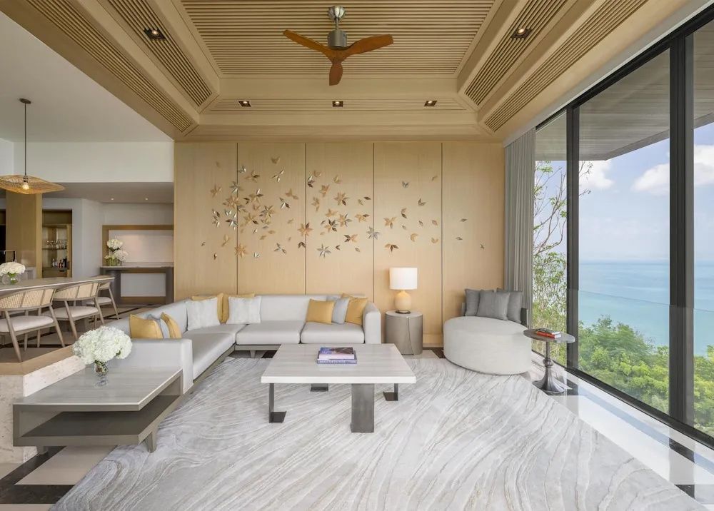 Heller Wohnbereich einer Villa mit großer Couch, Holzvertäfelung und Meerblick durch Panoramafenster.