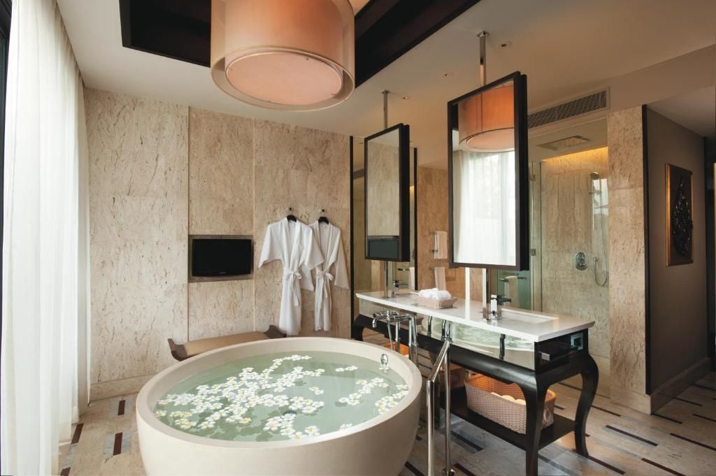 Runde freistehende Badewanne mit Blüten im Wasser und Doppelwaschtisch im Hotelbad.