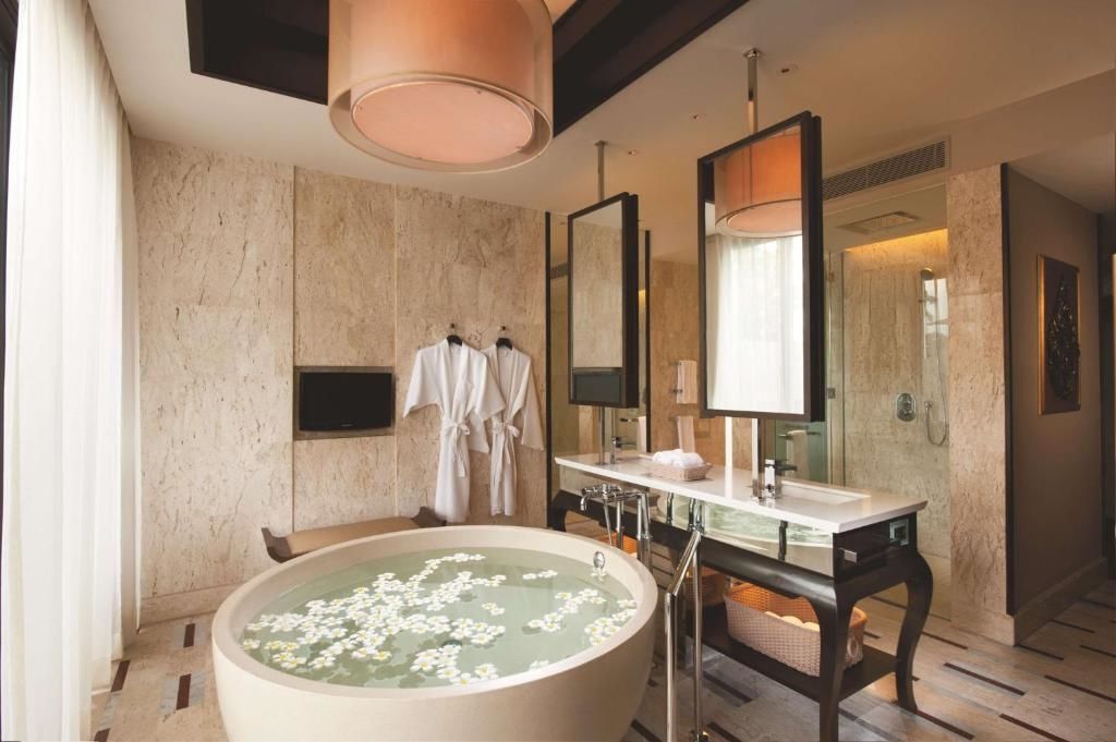 Badezimmer mit einer runden Badewanne voller Blüten und zweifachem Waschtisch.