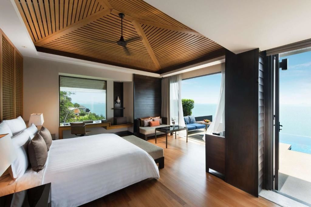 Geräumiges Hotelzimmer mit Holzdecke, Doppelbett, Sitzbereich und Zugang zur Terrasse mit Meerblick.