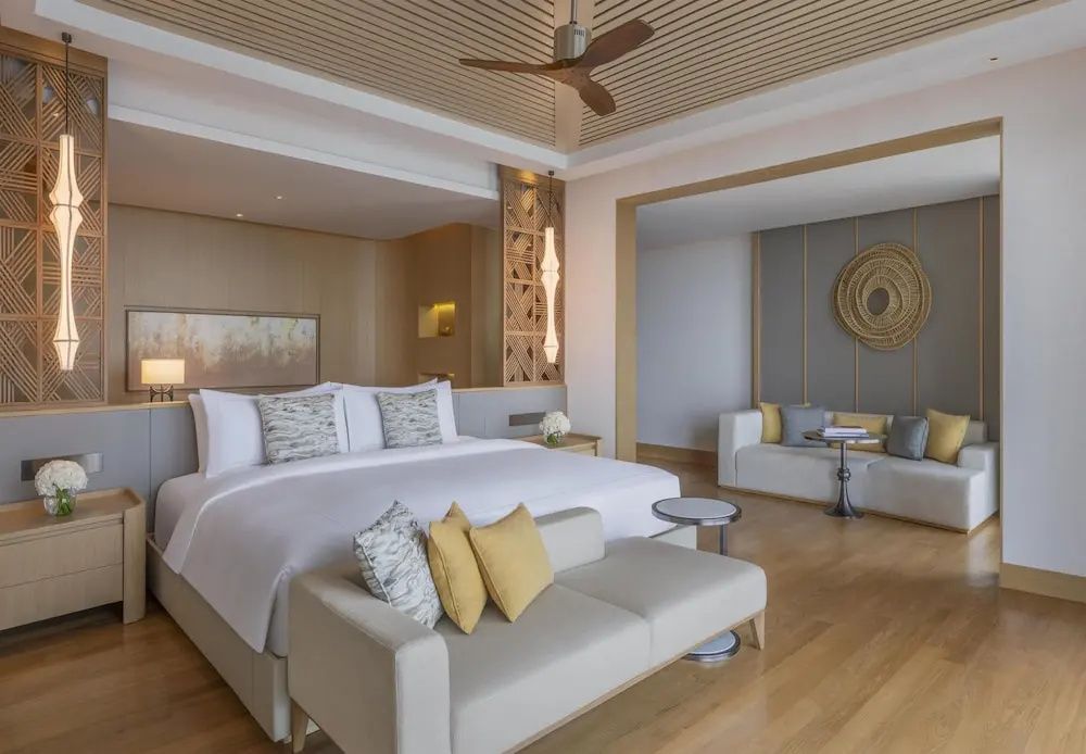 Helles Schlafzimmer mit Doppelbett, Sitzbank, Holzdecke mit Ventilator und angrenzender Lounge.