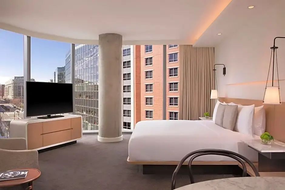 Hotelzimmer mit großem Doppelbett, Flachbildfernseher und bodentiefen Fenstern mit Stadtblick.