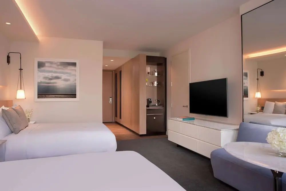 Hotelzimmer mit Betten, Fernseher auf weißer Kommode und Blick in den Flur.