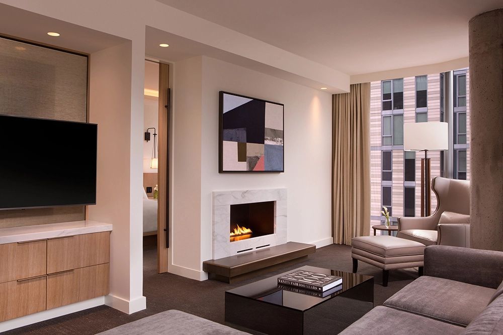 Modernes Wohnzimmer einer Suite mit Kamin, Sitzbereich und Blick zum Schlafbereich.