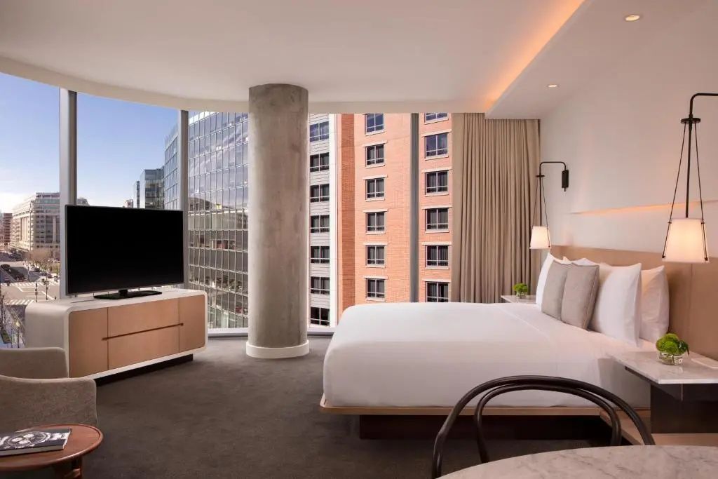 Doppelbett und Fernseher vor bodentiefen Fenstern mit Blick auf die Stadt.